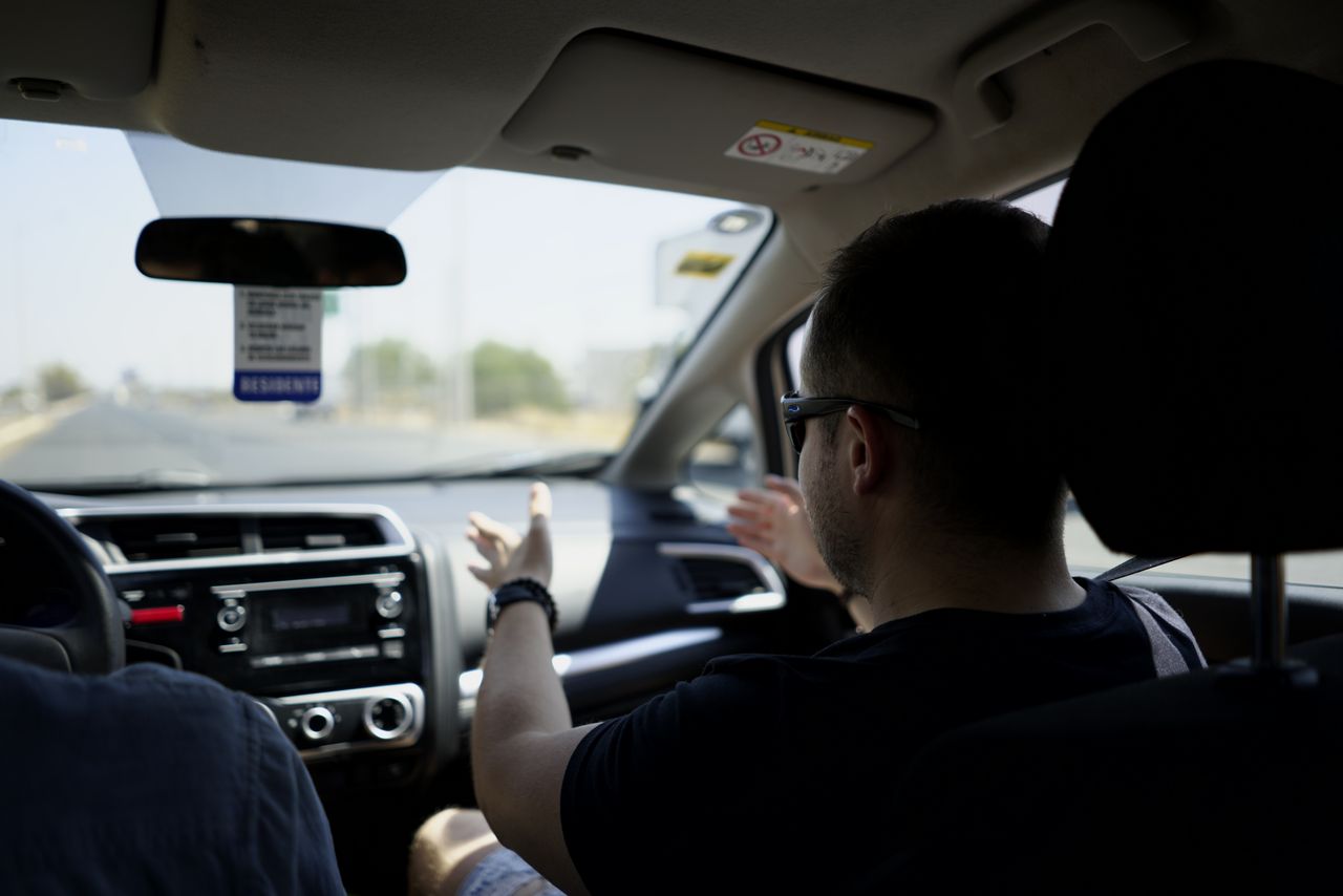 Passenger gesturing while conversing during a car journey on a sunny day.