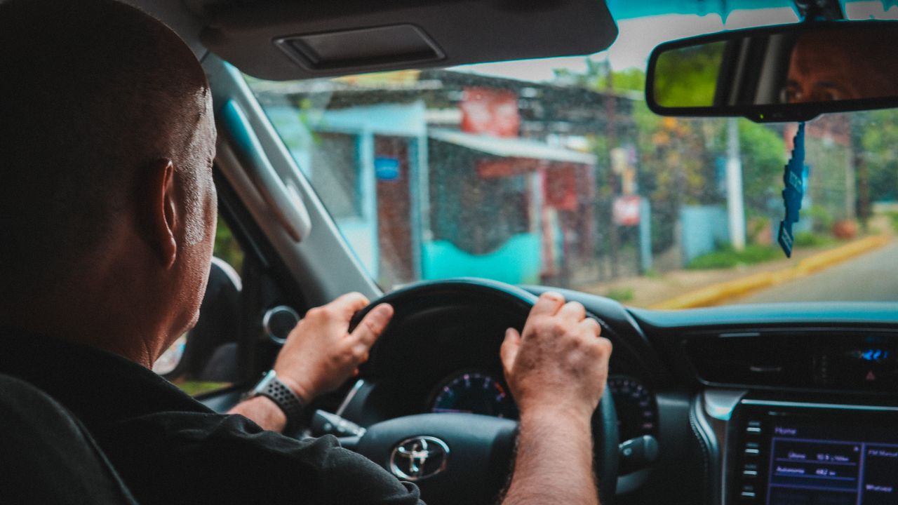 A man driving a car through San Juan del Sur, showcasing the city streets from the driver's perspective.