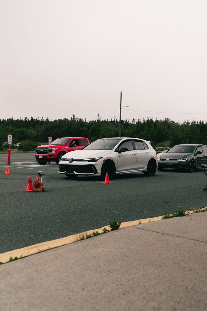 Vehicles on an outdoor driving course surrounded by traffic cones and greenery.