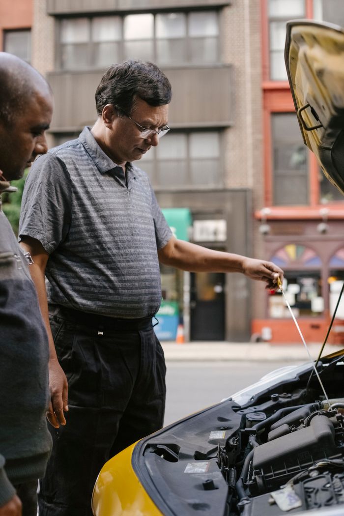 Side view of crop males checking and fixing engine of automobile on city street