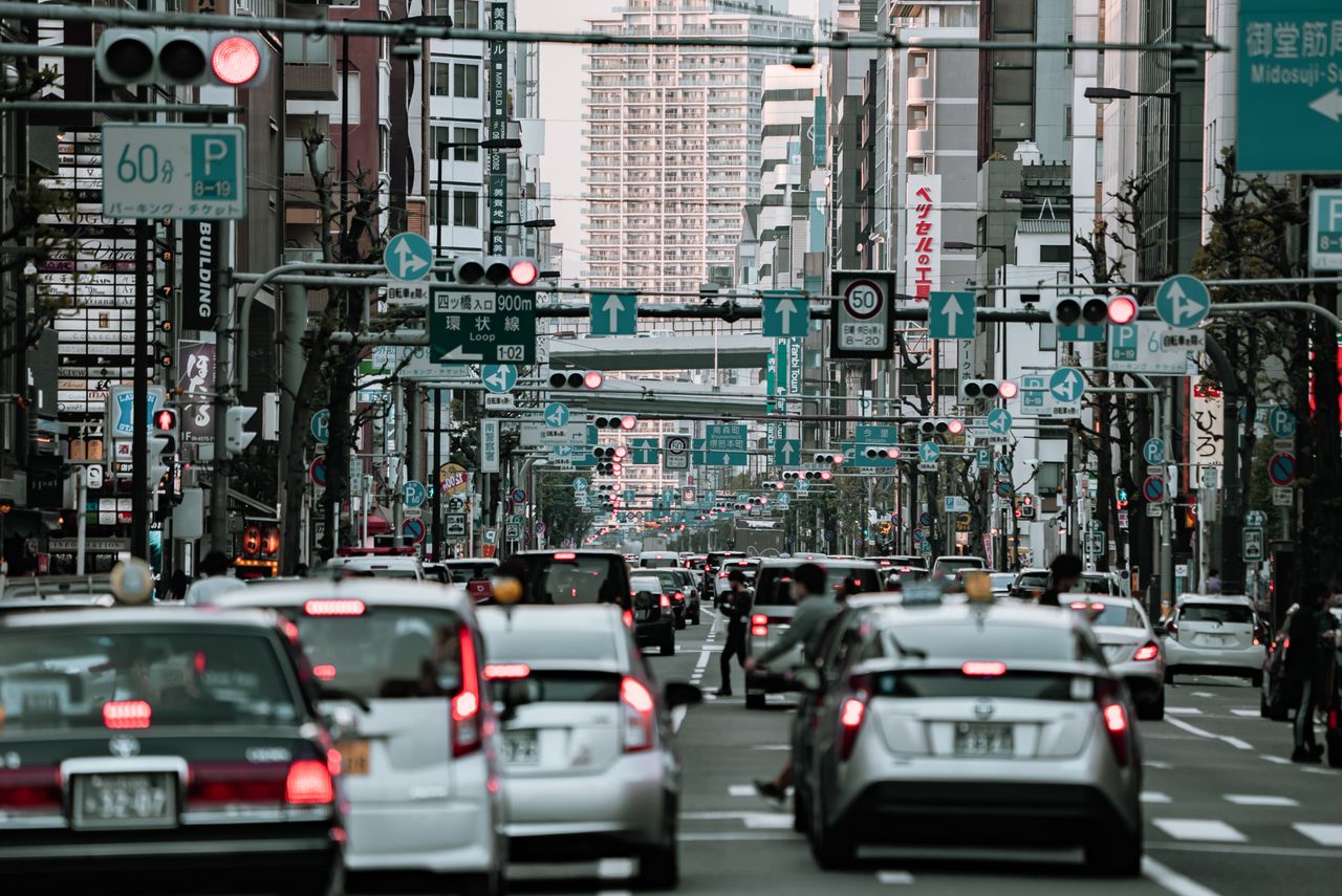 A bustling urban street in Osaka, Japan with heavy traffic and cityscape buildings in view.