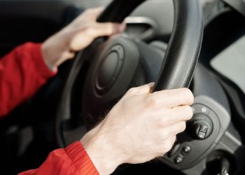 A person's hands gripping the steering wheel inside a vehicle, emphasizing safe driving.